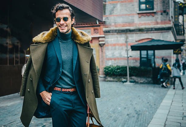 Handsome desirable gentleman in suit, out in the city. He is walking and carying a bag.