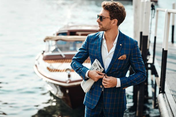 Young handsome man in classic suit over the blurred lake buttoning his jacket