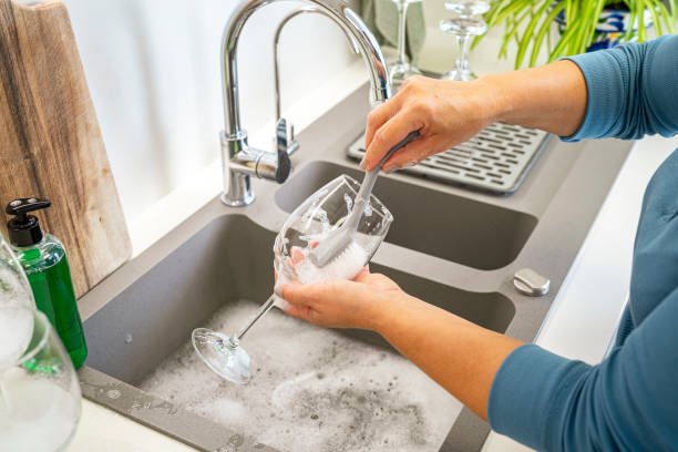 Woman washing wineglass with a scrubbing brush and soap in kitchen sink. High resolution 42Mp indoors digital capture taken with SONY A7rII and Zeiss Batis 40mm F2.0 CF lens