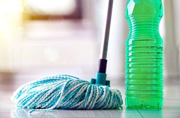 Plastic bottle with green disinfectant product for floor and mop with white and blue fiber strips reflected on white tiled tiles and background cooking. Front view.