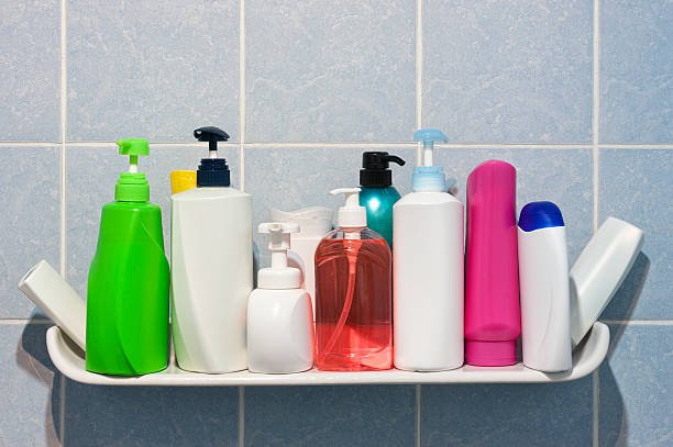Many shampoo and soap bottles on a bathroom or shower shelf.