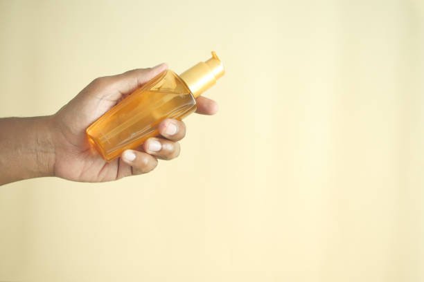 young man holding a hair oil against light yellow background .