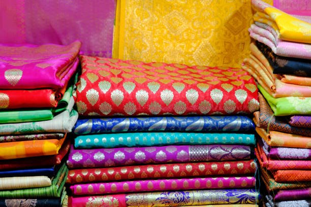 Artistic variety shade tone colors ornaments patterns, closeup view of stacked saris or sarees in display of retail shop.