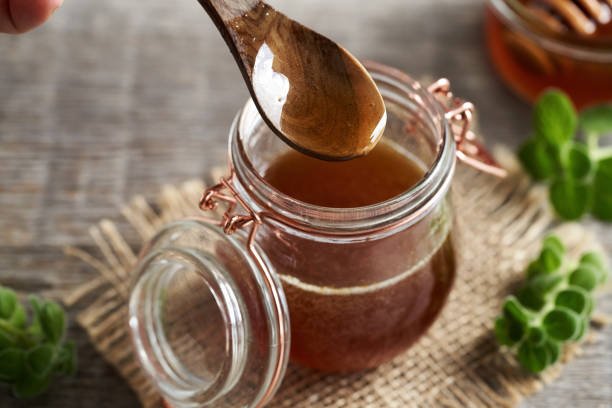 Plectranthus amboinicus syrup for common cold on a wooden spoon above a glass jar