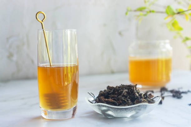 a glass of raw wild honey on white table with loose leave green tea and fermented Jun Tea jar.